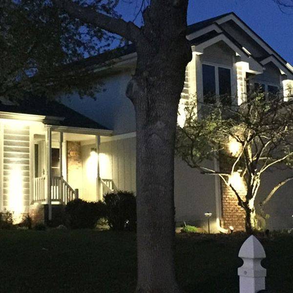 Lit home entrance with a tree and exterior landscape lighting at night.
