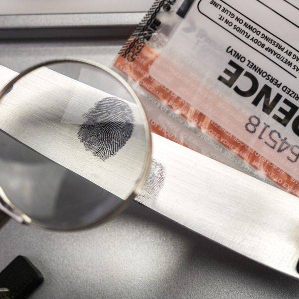 A magnifying glass resting on a fingerprint card next to an evidence tag.