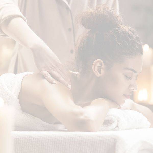 Client receiving a massage on a table in soft candlelit light with a therapist's hands on the back.