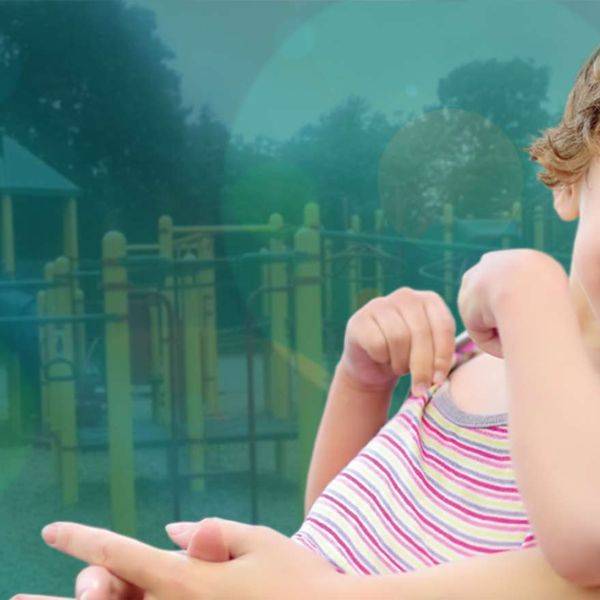 A smiling young child in a pink and white striped shirt, photographed outdoors.