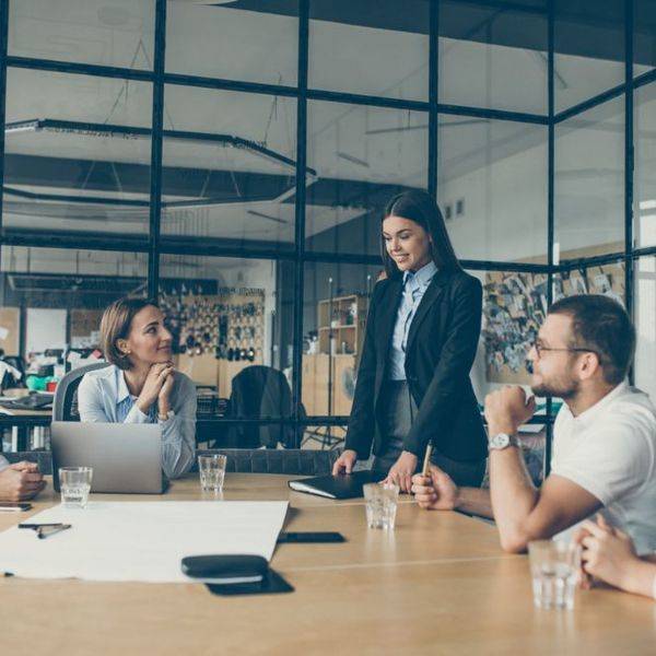 Colleagues gather around a glass-walled conference table during a meeting.