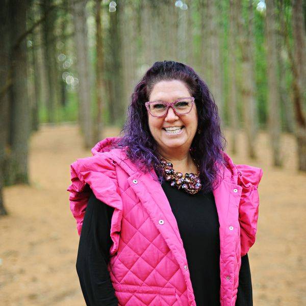 A smiling woman in a pink quilted vest stands outdoors against a blurred background.