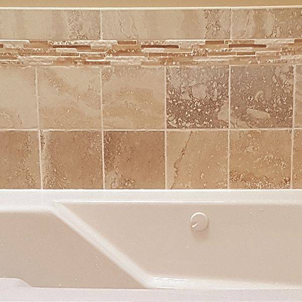 White bathtub with a tiled wall surround in beige and tan stone tones.