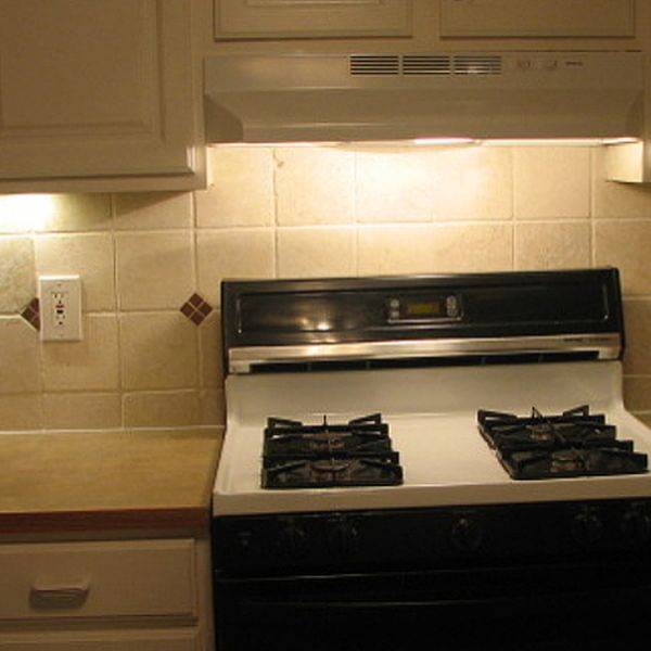 Kitchen range set between tiled backsplash with beige tiles and wood cabinets.