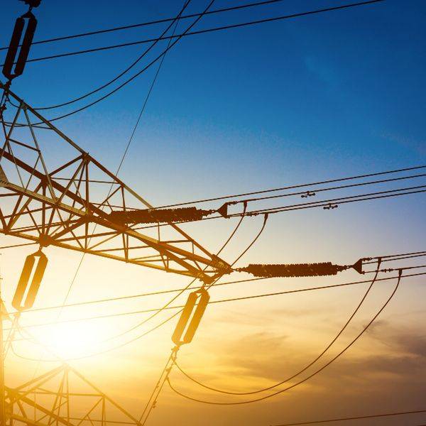 A high-voltage transmission tower and power lines silhouetted against a sunset sky.